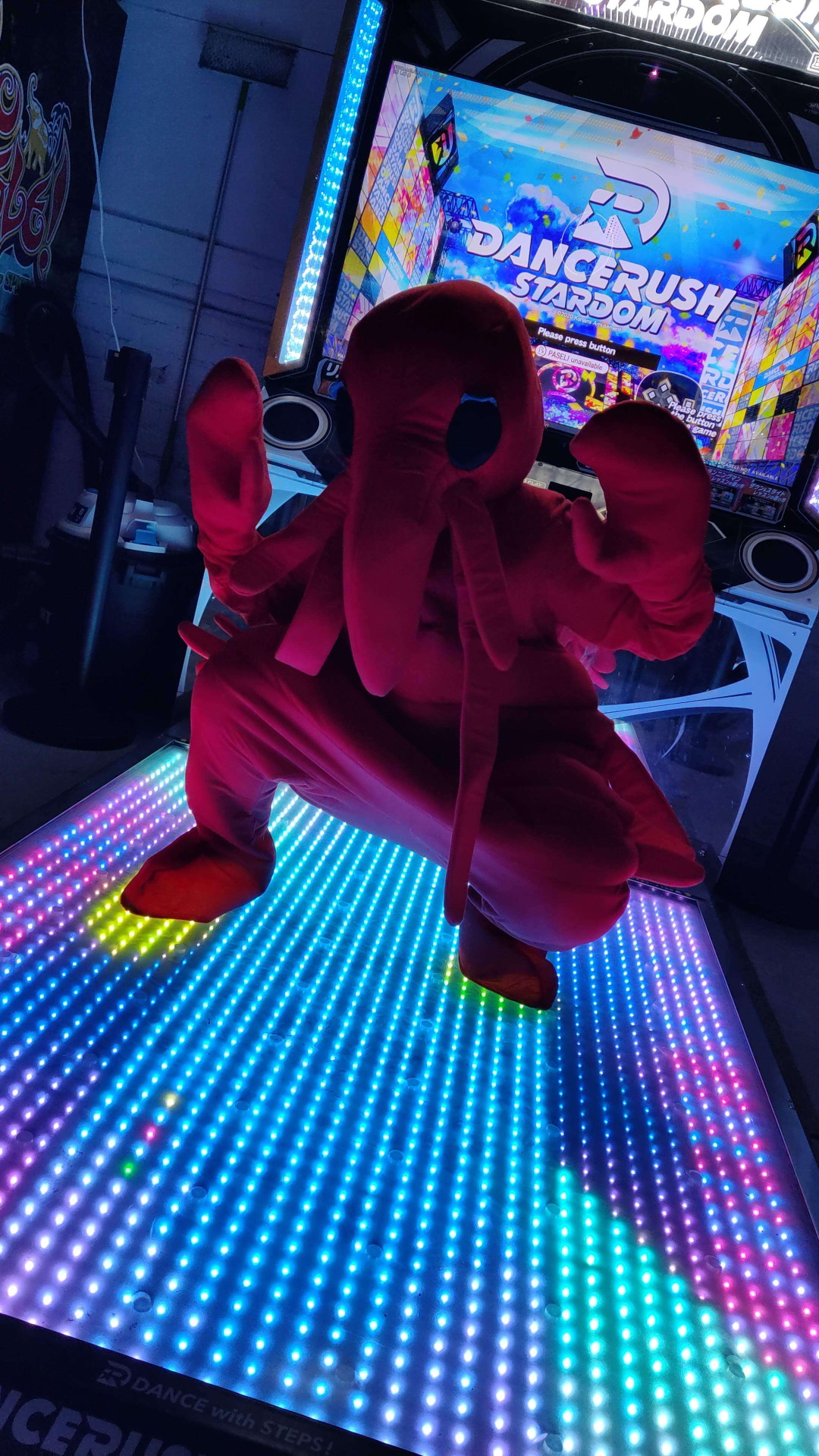 A person in a lobster costume standing on a Dancerush Stardom cabinet
