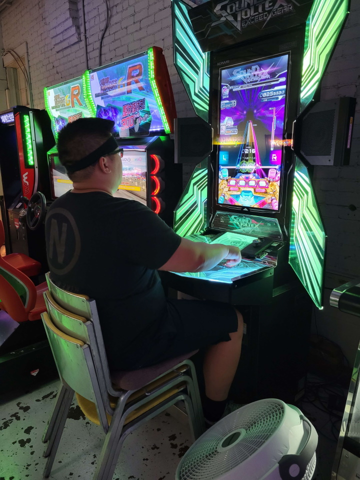 A man sitting on a stack of chairs playing Sound Voltex.