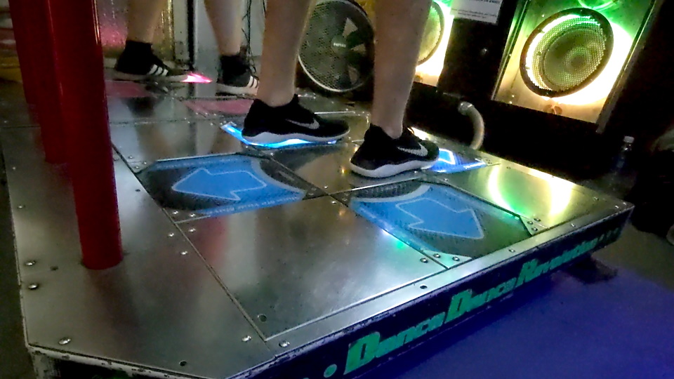 Close-up of two people dancing on a StepMania arcade game.